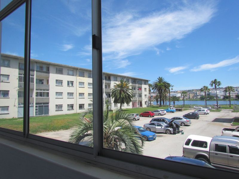 A view from an interior window overlooking the apartment complex grounds, parking area, and distant water.