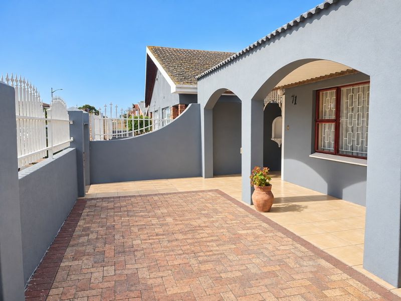A well-maintained front exterior featuring a paved driveway, a covered arched porch with tiled flooring, and secure perimeter walling with metal fencing.