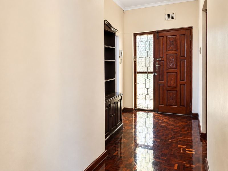 A welcoming entrance hall featuring polished parquet flooring and a classic solid wood front door with an integrated security gate.