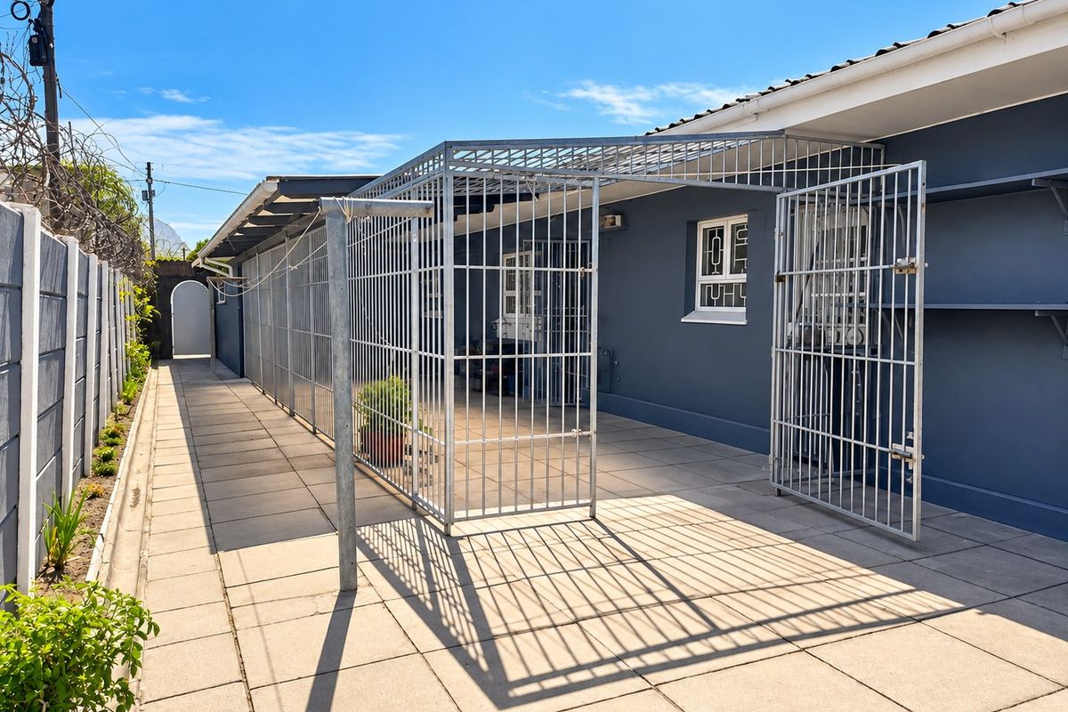A paved rear patio area featuring a secure metal enclosure, security gates, and perimeter walling with razor wire.