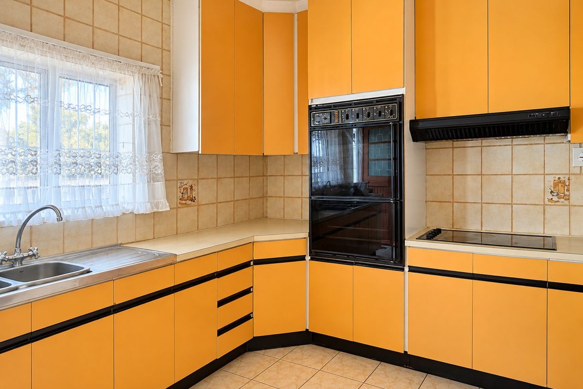 A functional kitchen featuring bright orange cabinetry, built-in oven, electric cooktop, extractor fan, and tiled finishes throughout.