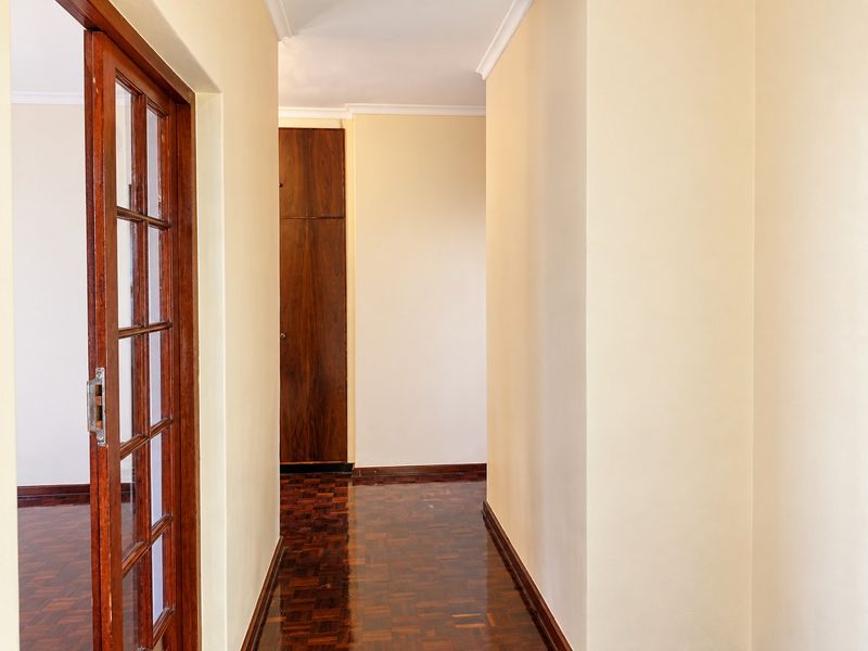 A clean, well-maintained hallway featuring polished parquet flooring, a built-in wooden cupboard, and a classic wooden-framed glass door.