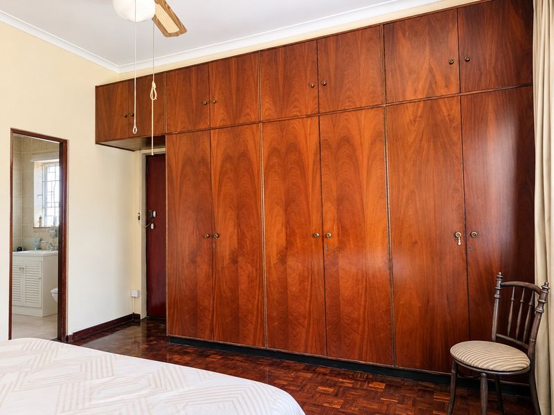 Bedroom featuring extensive floor-to-ceiling built-in wooden cabinetry, classic parquet flooring, and a ceiling fan, with an adjoining en-suite bathroom visible.