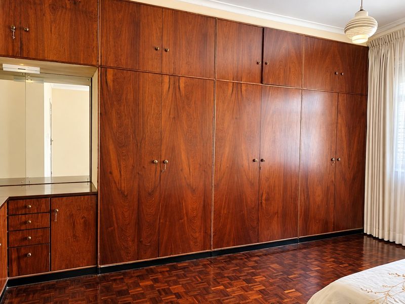 Bedroom featuring extensive floor-to-ceiling built-in wooden cabinetry with integrated vanity and classic parquet flooring.