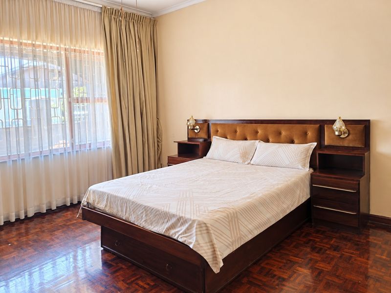 A well-maintained bedroom featuring classic parquet flooring, a built-in headboard with integrated bedside tables, and wall-mounted lighting.