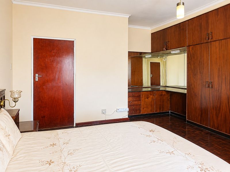 Spacious bedroom featuring extensive built-in wooden cabinetry, a integrated vanity area with mirror, and traditional parquet flooring.