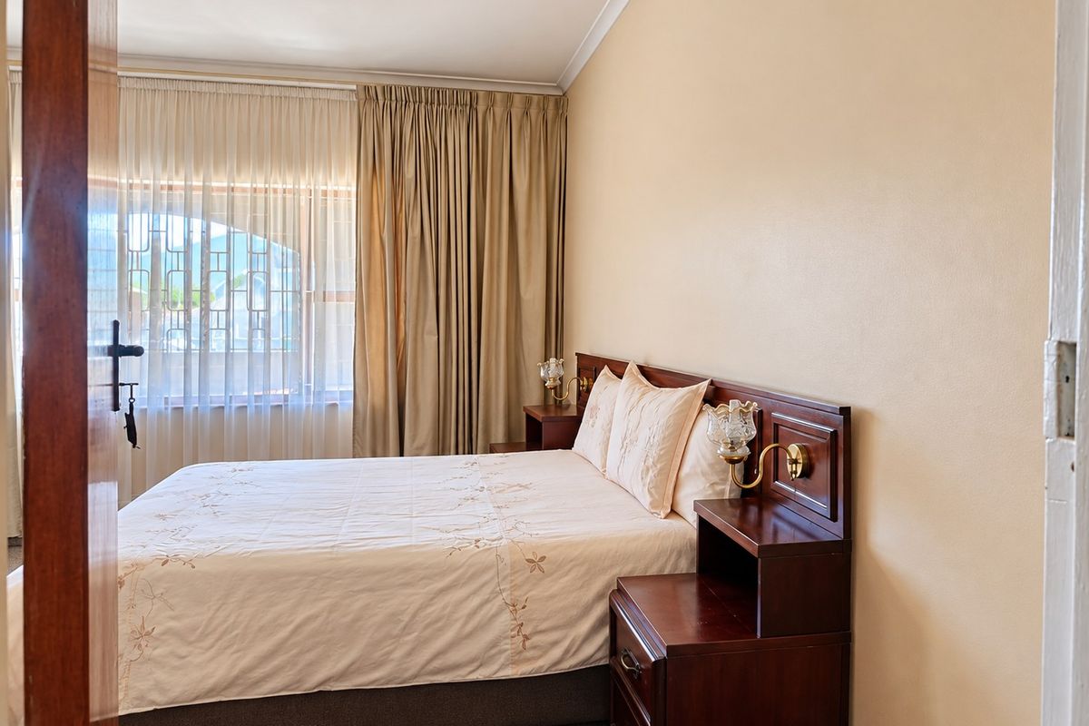 A well-maintained bedroom featuring a built-in wooden headboard with integrated bedside tables and wall-mounted lighting, offering a functional and classic layout.