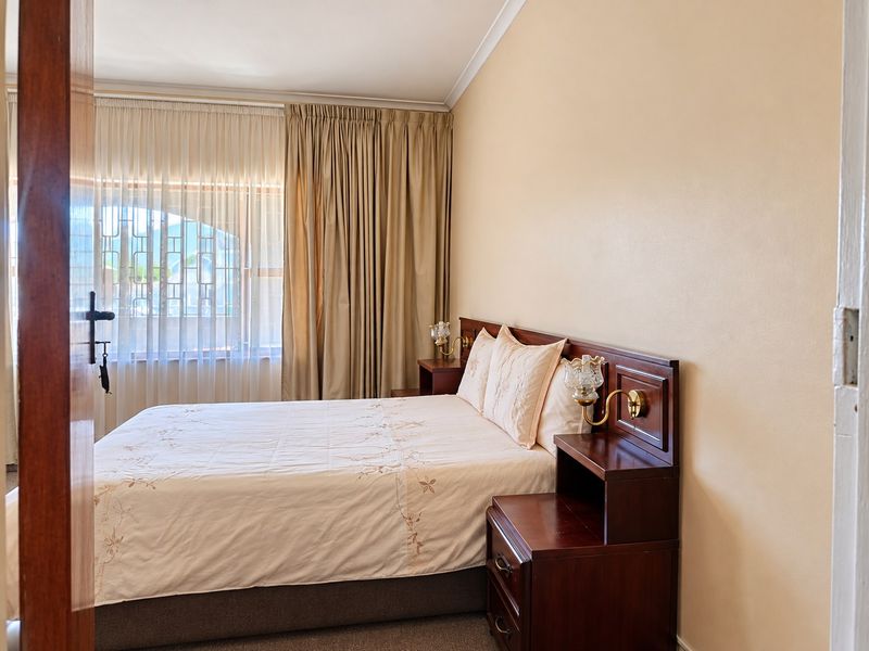 A well-maintained bedroom featuring a built-in wooden headboard with integrated bedside tables and wall-mounted lighting, offering a functional and classic layout.