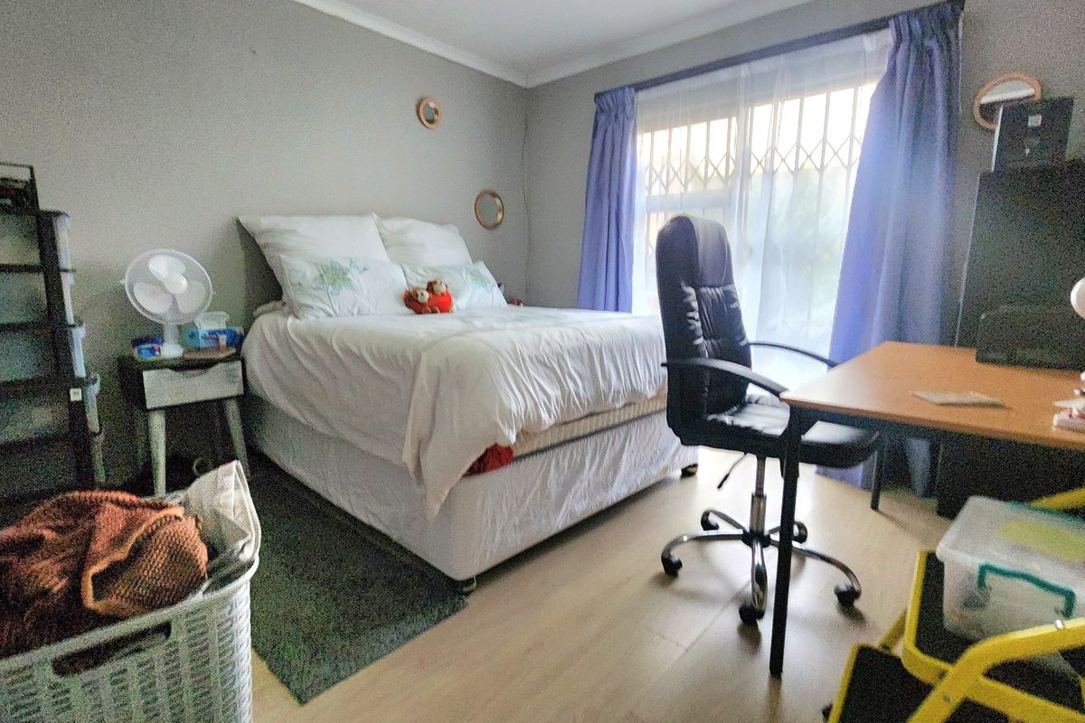 A functional bedroom featuring light-toned laminate flooring, a window with a security gate, and neutral wall finishes.
