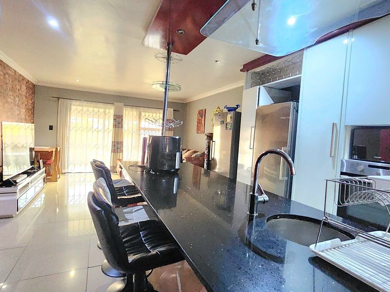 Spacious open-plan living area featuring a modern kitchen with a large granite island, high-gloss cabinetry, and integrated appliances, flowing into the lounge space.