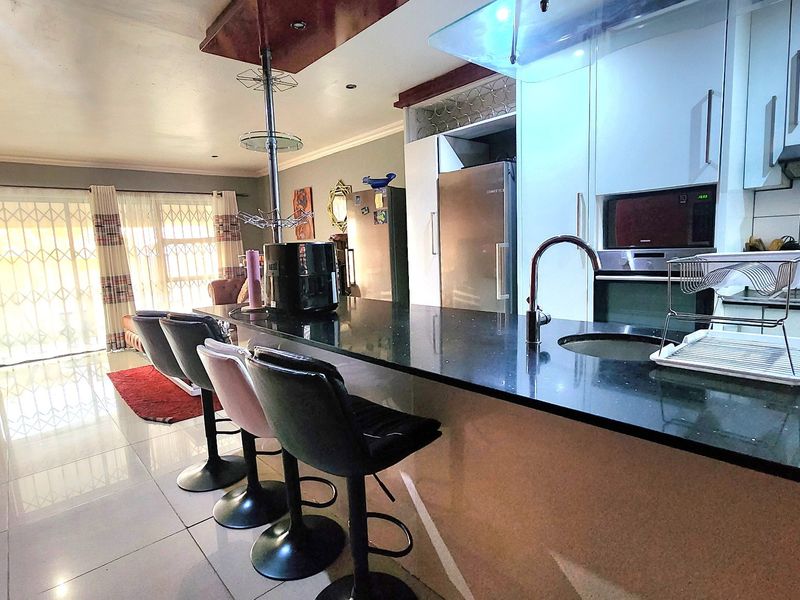Open-plan living and kitchen area featuring a granite island, built-in appliances, tiled flooring, and access to the exterior through a security gate.