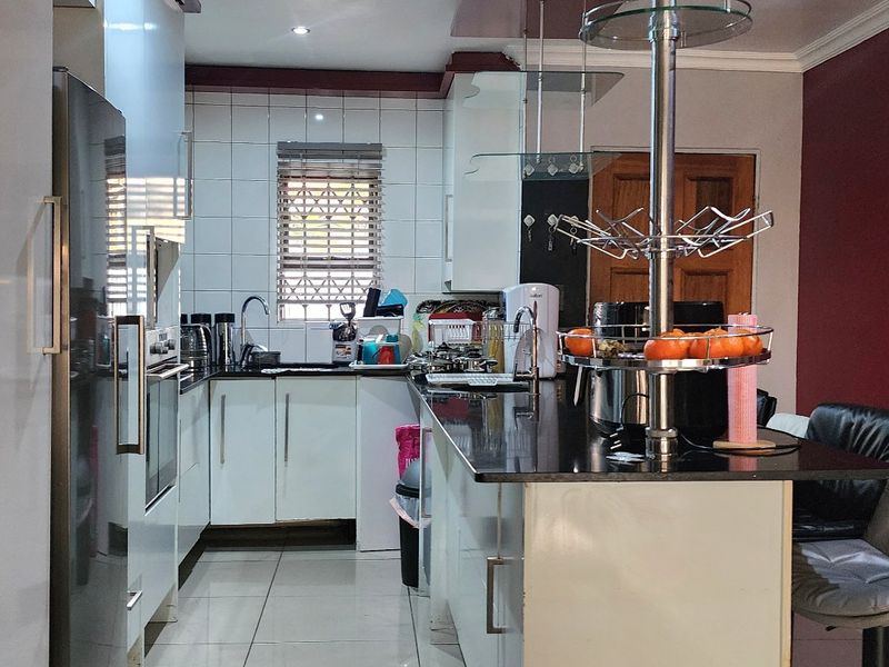 A functional kitchen featuring white cabinetry, dark granite countertops, a breakfast bar, and tiled flooring with integrated lighting.