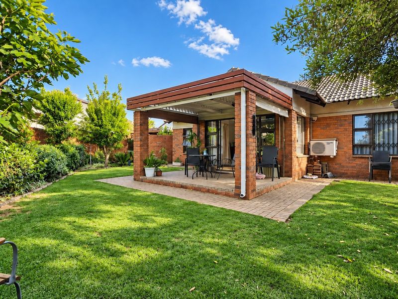 A well-maintained rear exterior featuring a brick townhouse facade, a covered patio area, and a neatly landscaped garden with a lush lawn.