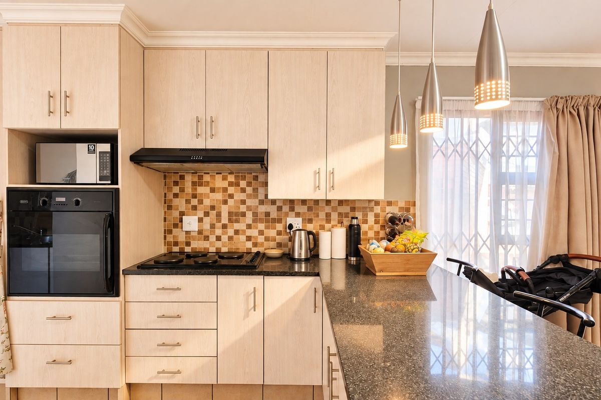 Modern kitchen featuring light wood cabinetry, granite countertops, mosaic tile backsplash, and integrated appliances including an oven, hob, and microwave.