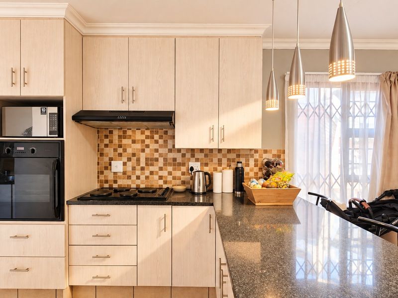 Modern kitchen featuring light wood cabinetry, granite countertops, mosaic tile backsplash, and integrated appliances including an oven, hob, and microwave.