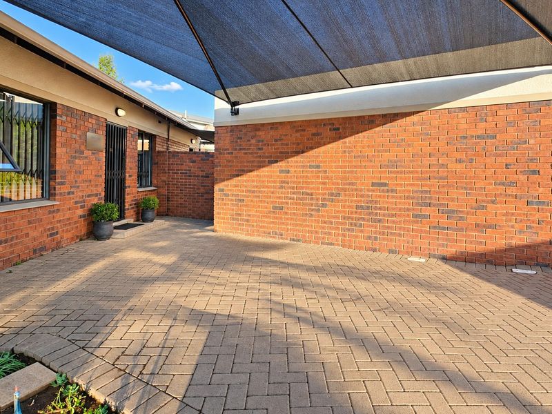 A well-maintained paved front courtyard area featuring face brick walls, a security gate, and a large overhead shade sail for protection.