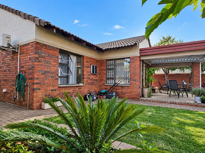 Rear view of the townhouse featuring a brick facade, a covered patio area, and a well-maintained garden with paved pathways.