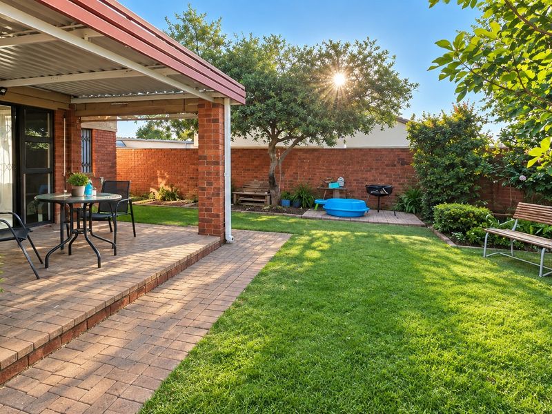 A well-maintained private garden featuring a covered brick-paved patio, lush lawn, and secure brick boundary walls, perfect for outdoor relaxation.