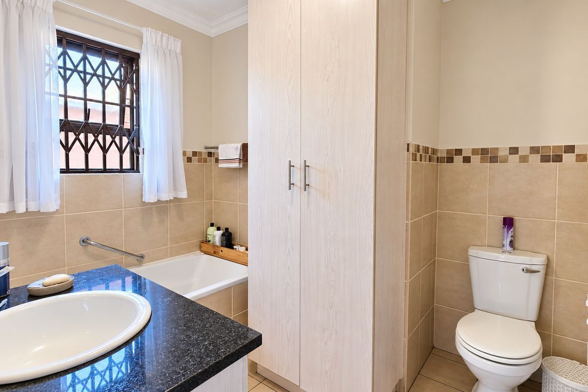 A well-maintained bathroom featuring a granite-topped vanity, built-in storage cupboard, bathtub, and tiled wall finishes.