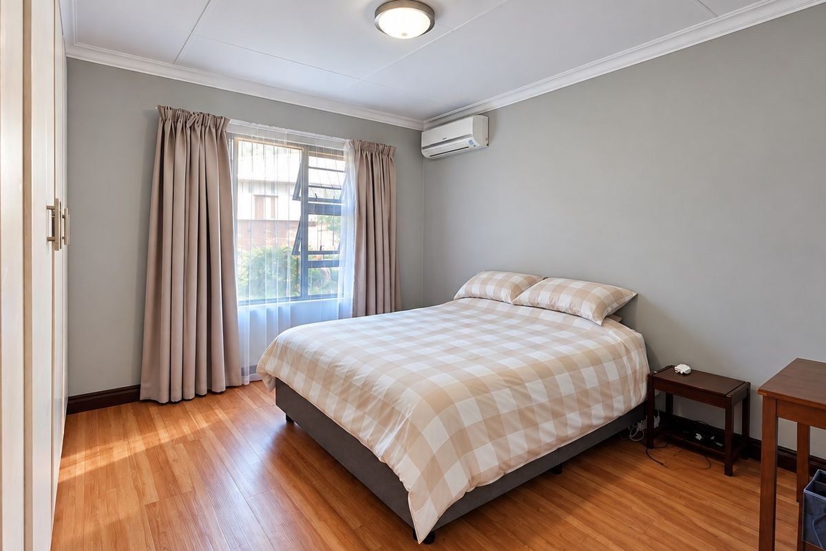 A well-maintained bedroom featuring laminate flooring, built-in cupboards, and a wall-mounted air conditioning unit.
