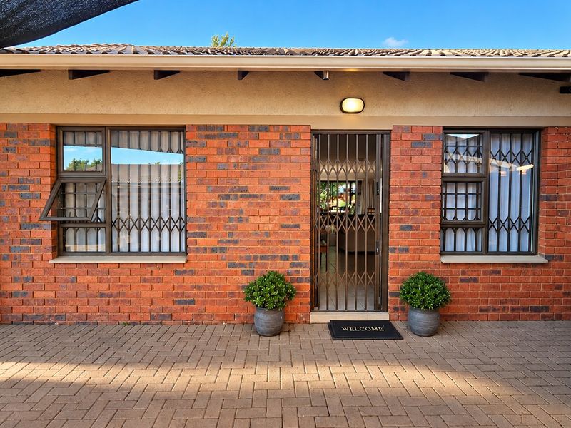 Front entrance of a townhouse featuring a face brick facade, paved driveway, and secure metal security gate and window bars.