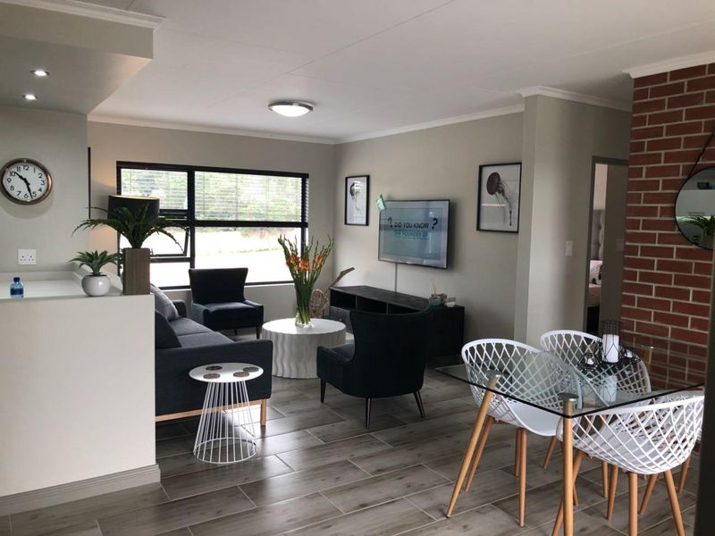 Spacious open-plan living and dining area featuring modern tiled flooring, an exposed brick feature wall, and ample natural light through large windows.