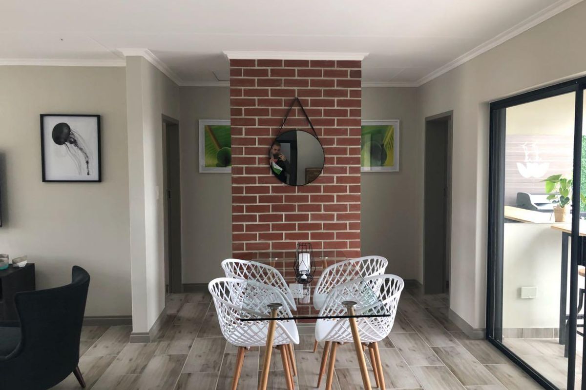 A well-lit dining area featuring a distinctive exposed brick feature wall, modern tiled flooring, and direct access to an outdoor patio through sliding glass doors.