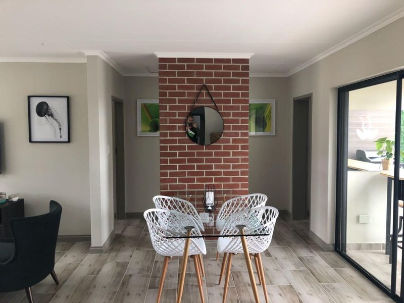 A well-lit dining area featuring a distinctive exposed brick feature wall, modern tiled flooring, and direct access to an outdoor patio through sliding glass doors.