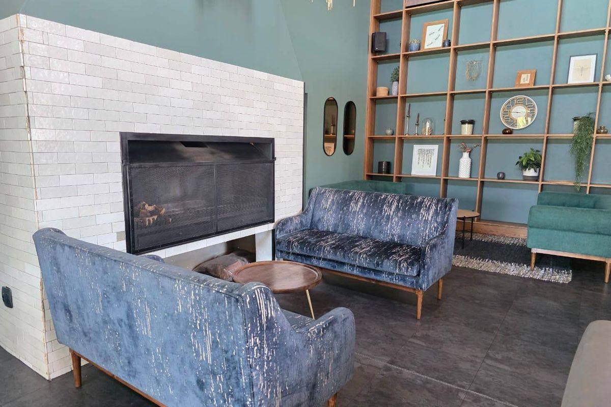 A stylish living room featuring a prominent white tiled fireplace and a large, built-in floor-to-ceiling wooden shelving unit against a deep green wall.