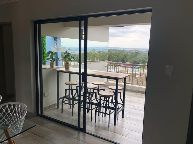 A modern balcony featuring tiled flooring, a metal balustrade, and sliding glass doors, offering an elevated view of the surrounding landscape.