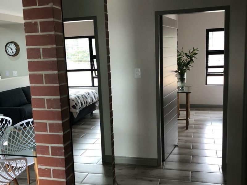 A well-maintained hallway featuring modern tiled flooring, an exposed brick pillar, and a full-length mirror, providing access to adjacent living and bedroom areas.