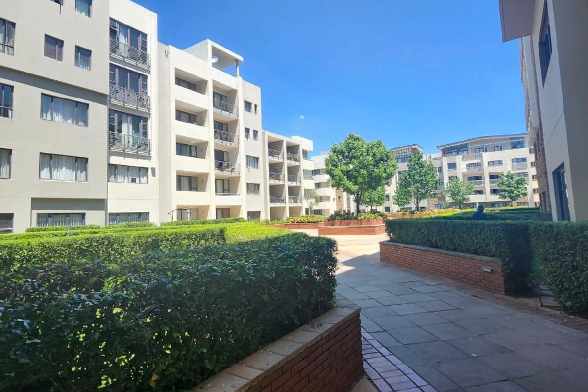 A well-maintained communal courtyard area featuring paved walkways, brick retaining walls, and manicured hedges between multi-story townhouse blocks.