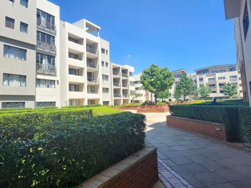 A well-maintained communal courtyard area featuring paved walkways, brick retaining walls, and manicured hedges between multi-story townhouse blocks.