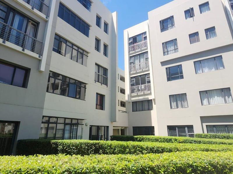 Exterior view of a modern townhouse complex featuring multi-story residential blocks with balconies and well-maintained landscaped hedges.