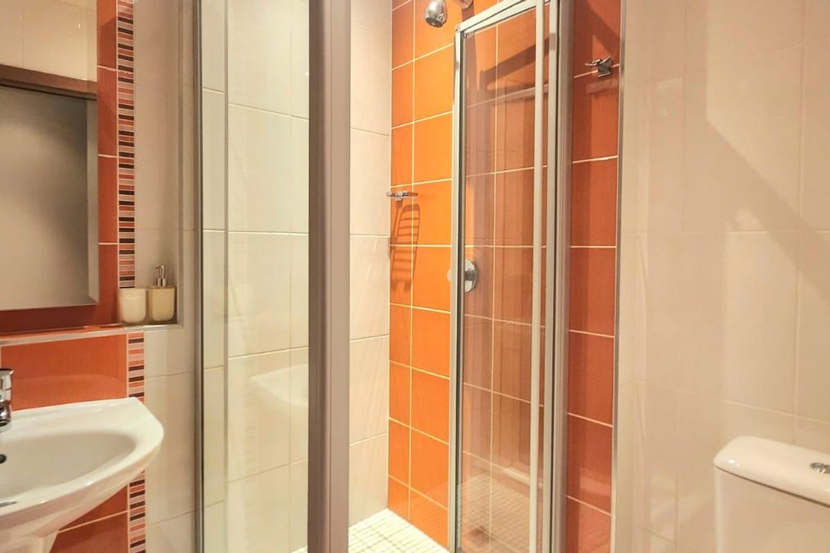 A functional bathroom featuring a shower enclosure, pedestal washbasin, and toilet with orange and white tiled wall finishes.