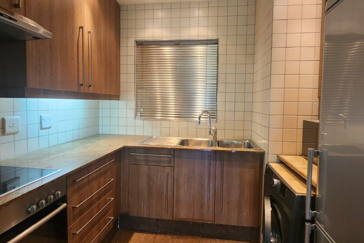 A functional kitchen featuring wood-finish cabinetry, tiled backsplash, integrated oven and hob, and a stainless steel sink with a window view.