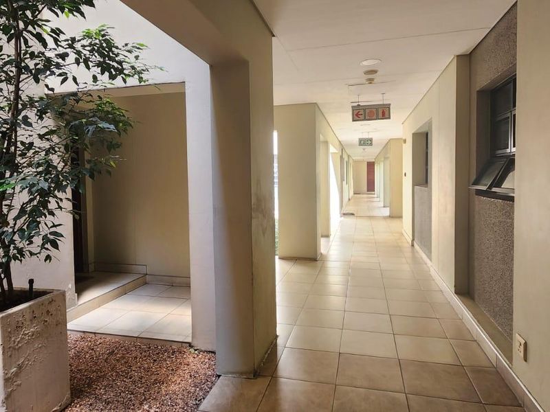 A well-lit, tiled communal hallway featuring concrete structural columns and emergency exit signage, providing access to residential units.