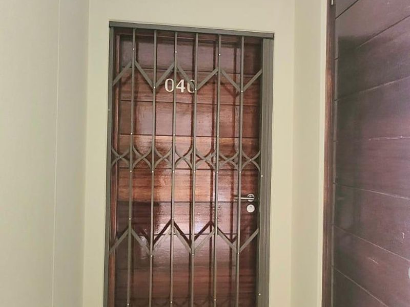 A clean and secure entrance area featuring a solid wood door with a protective security gate and neutral tiled flooring.