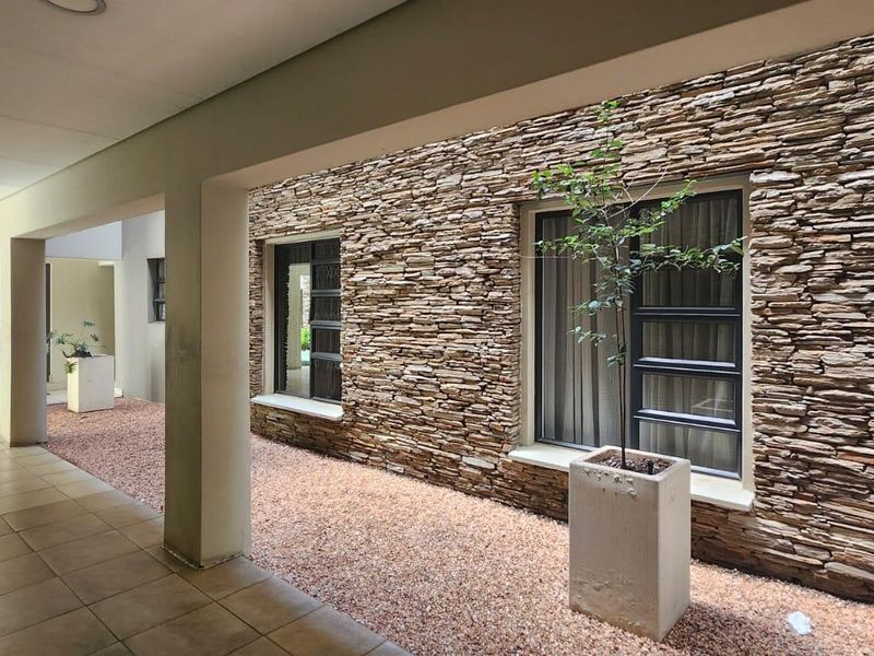 A covered outdoor walkway featuring decorative stone cladding, tiled flooring, and modern aluminium window frames, providing a clean and well-maintained transition space.