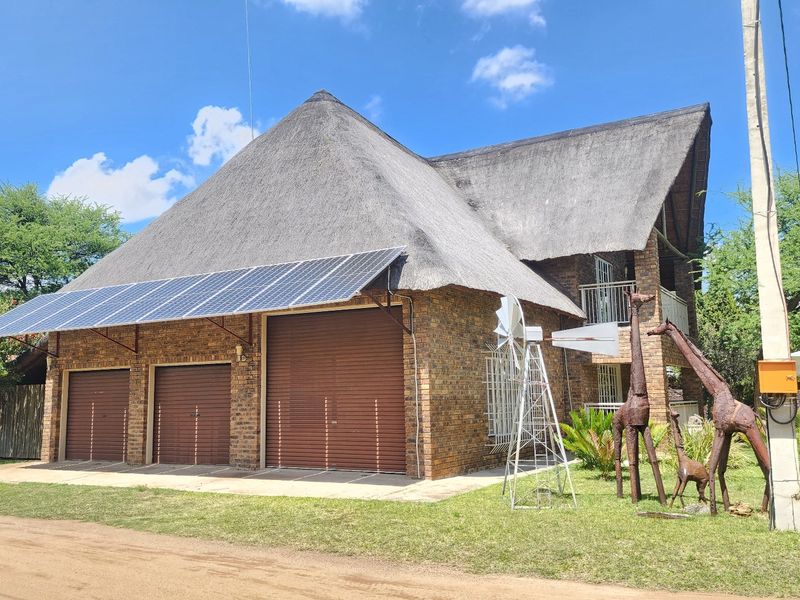 A double-story face brick house featuring a traditional thatch roof, a triple garage, and an integrated solar panel system.