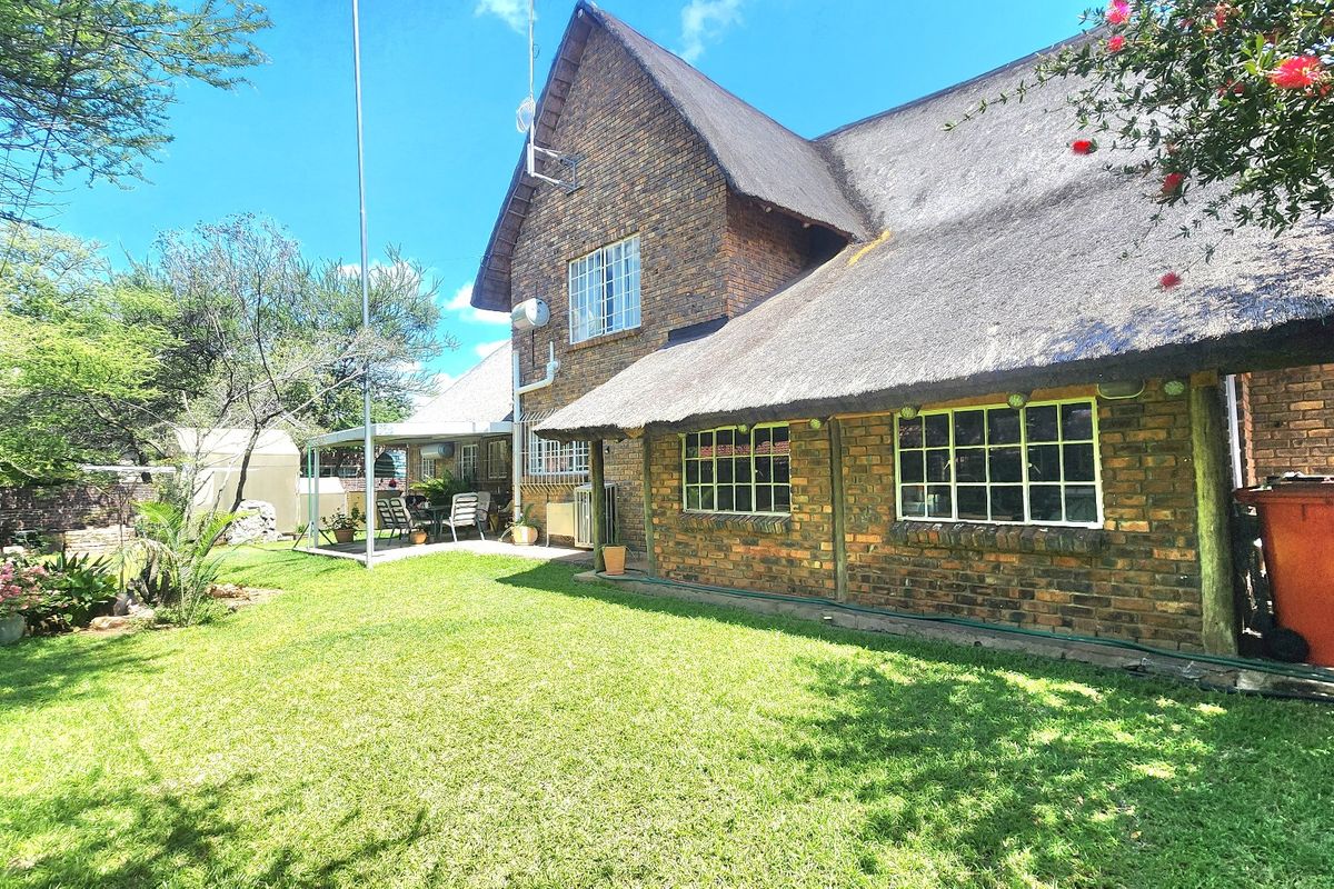 Rear view of a face brick house featuring a traditional thatch roof, covered patio area, and a well-maintained garden lawn.