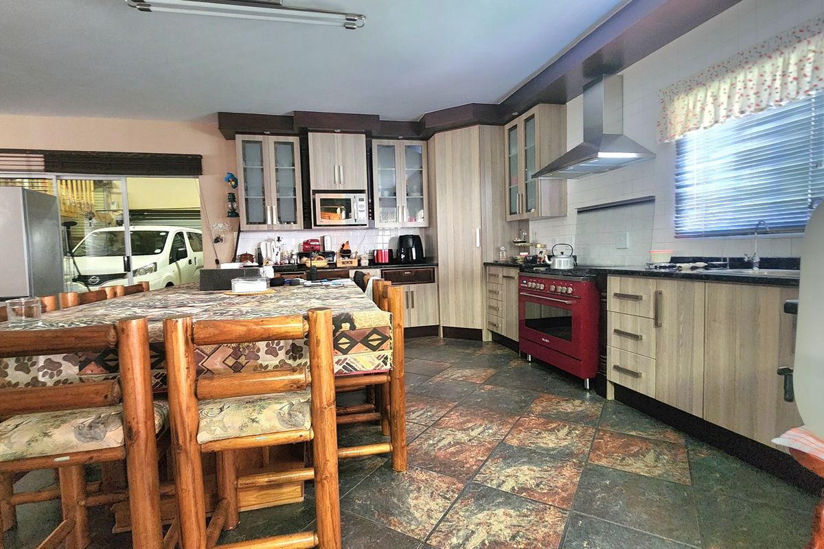 A functional kitchen featuring wood-look cabinetry, a red freestanding oven, extractor fan, and durable stone tile flooring.