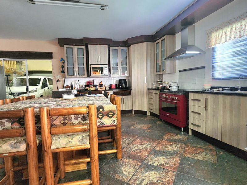 A functional kitchen featuring wood-look cabinetry, a red freestanding oven, extractor fan, and durable stone tile flooring.