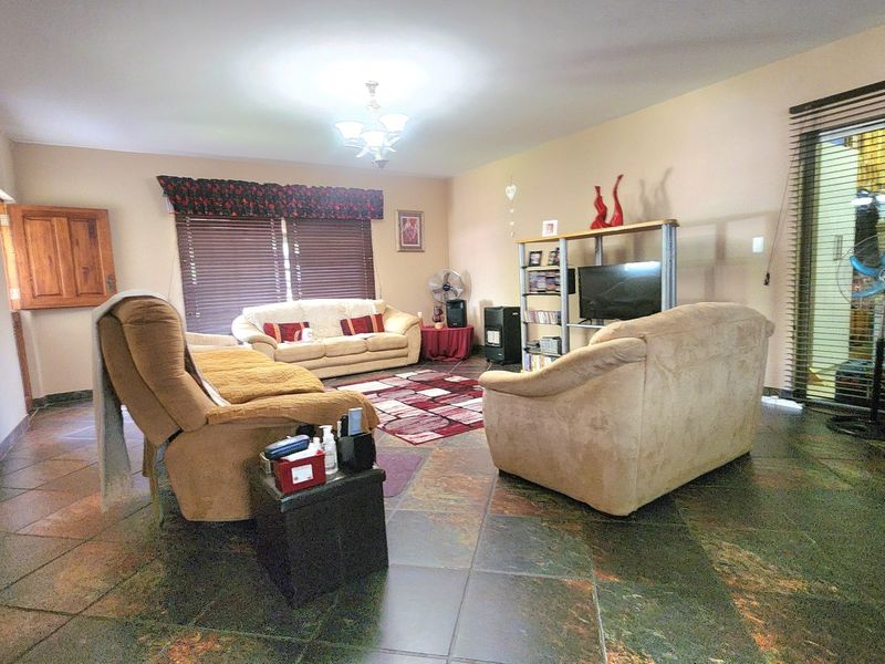 A spacious living room featuring slate tile flooring, large windows with venetian blinds, and a sliding glass door providing access to the exterior.