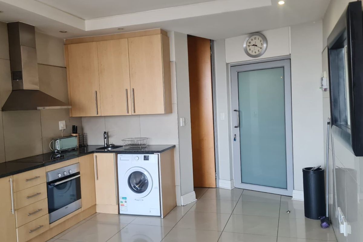 Modern kitchen featuring light wood cabinetry, dark countertops, built-in oven, stainless steel extractor fan, and integrated washing machine with tiled flooring.