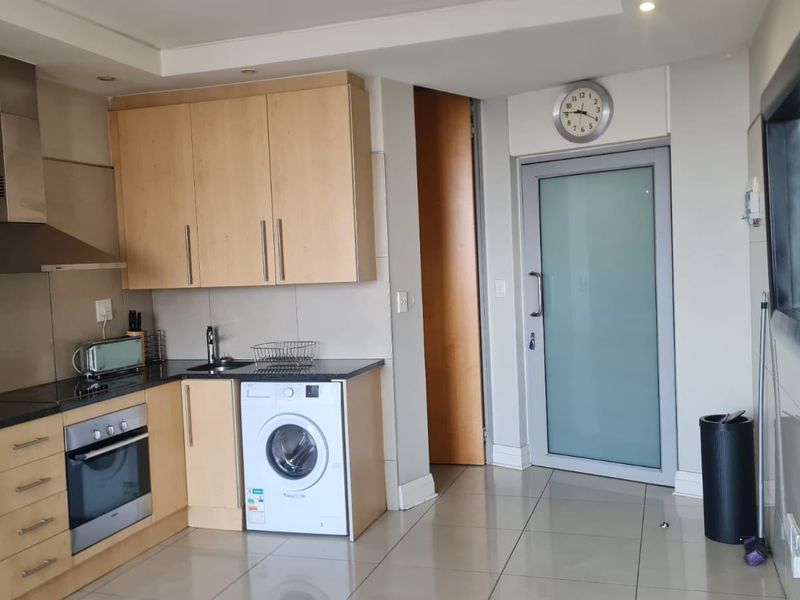 Modern kitchen featuring light wood cabinetry, dark countertops, built-in oven, stainless steel extractor fan, and integrated washing machine with tiled flooring.