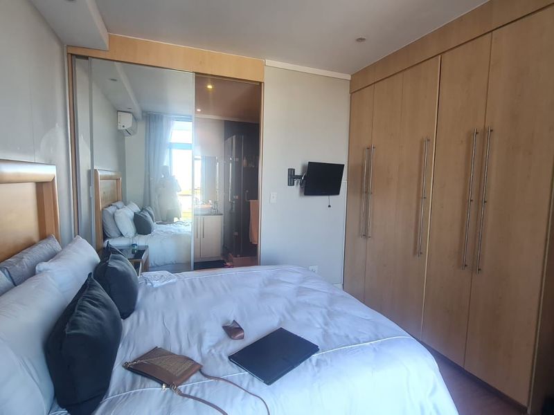 A well-maintained bedroom featuring extensive built-in wooden cupboards with mirrored sliding doors, recessed ceiling lighting, and an integrated air conditioning unit.
