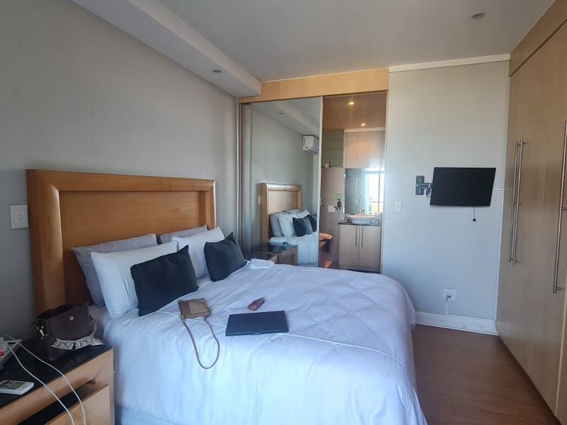A well-maintained bedroom featuring laminate flooring, extensive built-in cupboards with mirrored doors, and direct access to an en-suite bathroom.