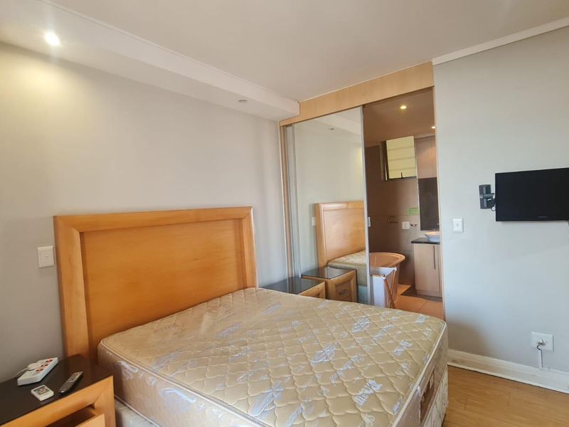 Bedroom featuring laminate flooring, built-in mirrored wardrobes, and an integrated air conditioning unit, with an adjoining en-suite bathroom visible through the sliding doors.