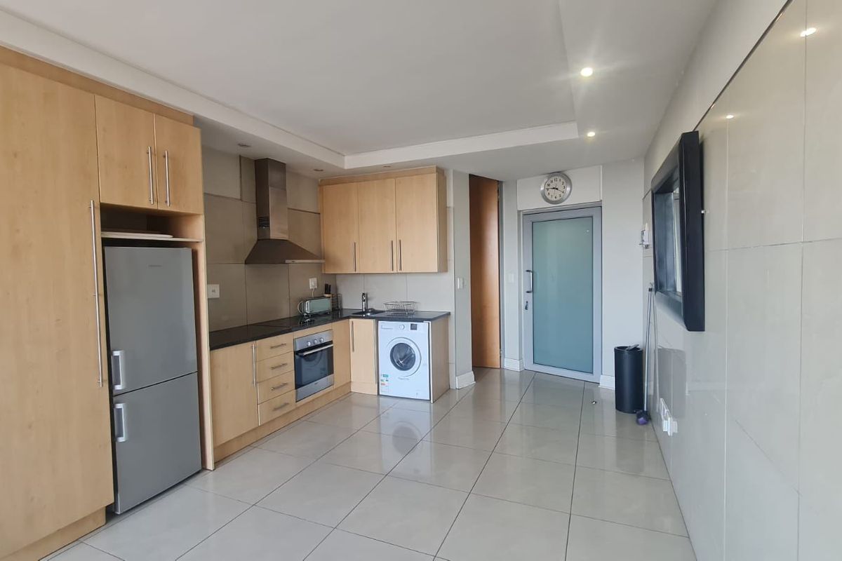 A modern kitchen featuring light wood cabinetry, stainless steel appliances, tiled flooring, and a sleek frosted glass door leading to the rest of the apartment.